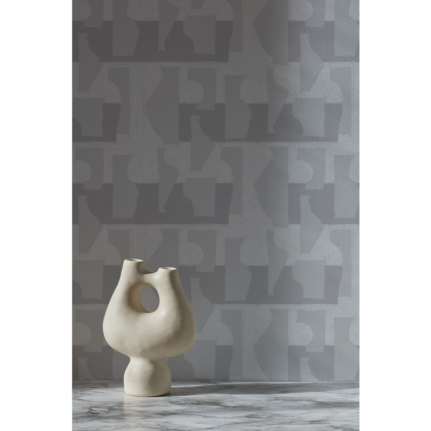 White vase in front of a wall with a pattern of pale grey geometric vessel shapes over a white background with soft grey horizontal stripes.