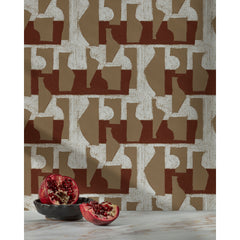 Pomegranate in a ceramic bowl in front of a wall with a pattern of taupe geometric vessel shapes over a white background with brick red horizontal stripes.