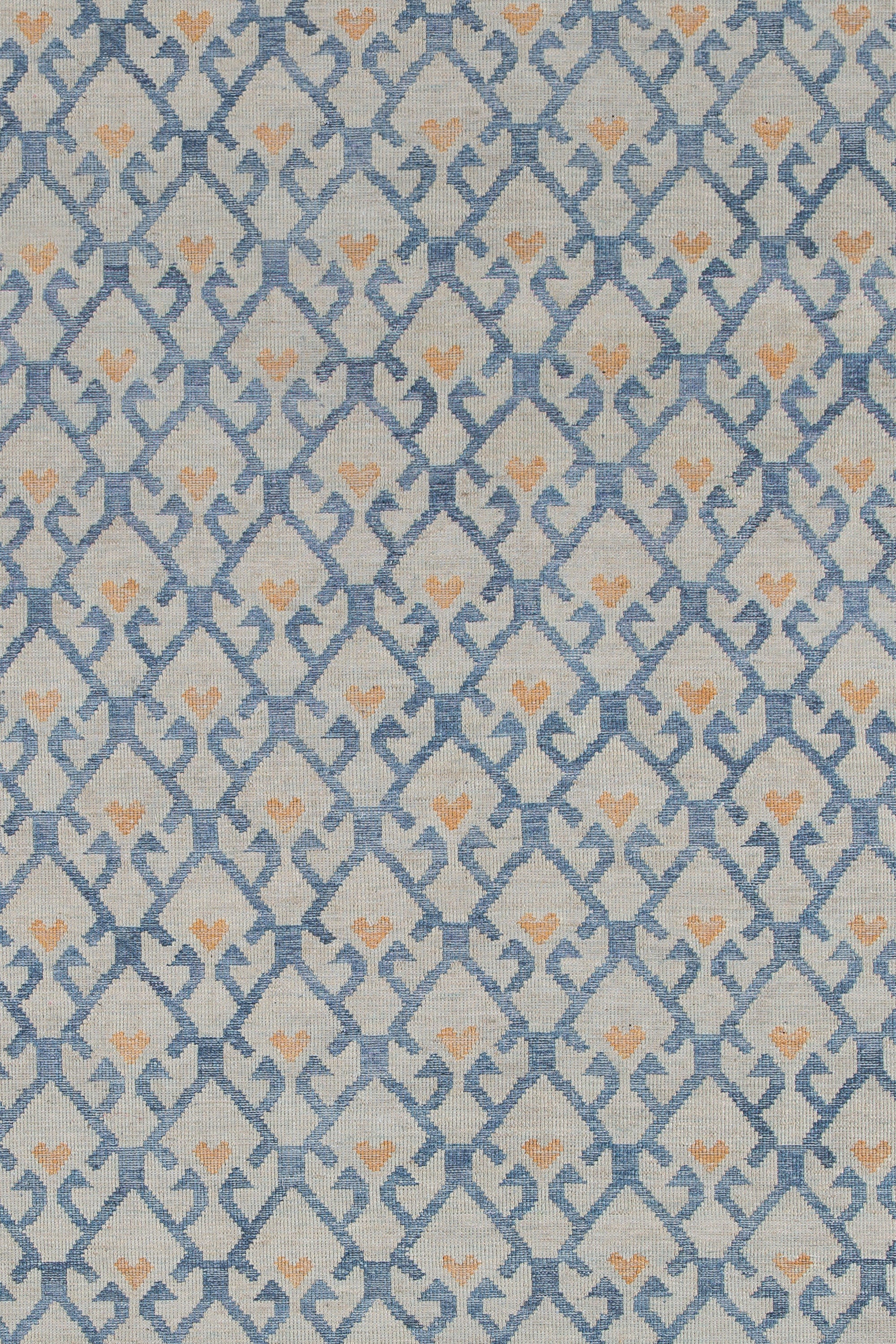 Detail of the Avesta Rug in Blue, a blue lattice pattern on a beige field with small orange heart accents. 
