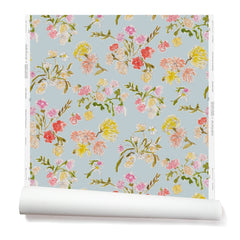 Partially unrolled wallpaper with a pattern of large-scale line-drawn flowers in gray ink with red, pink and yellow watercolors, on a light blue background.