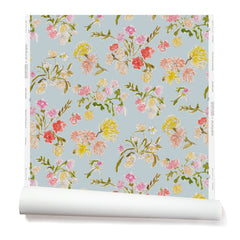 Partially unrolled wallpaper with a pattern of large-scale line-drawn flowers in gray ink with red, pink and yellow watercolors, on a light blue background.
