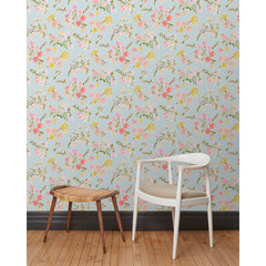 A chair and stool stand in front of a wall papered in large-scale line-drawn flowers in gray ink with red, pink and yellow watercolors, on a light blue background.