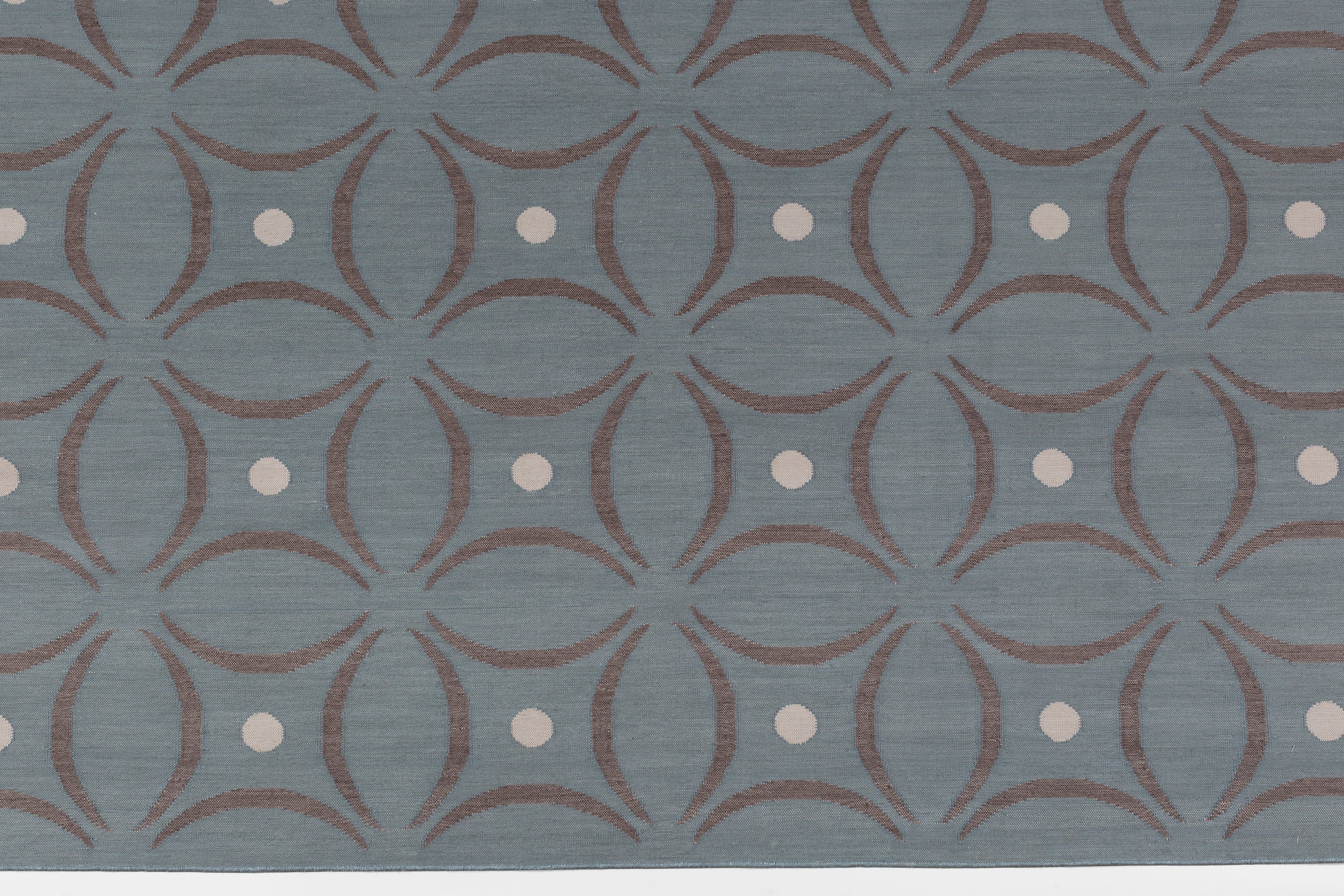 Detail of the Boe rug in Argento, featuring a pattern of curved segments in grey with white circles on a blue field. 