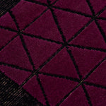 Detail of the Bucky Rug in berry, features a wide black border with a wine colored lattice field with a metallic sheen. 