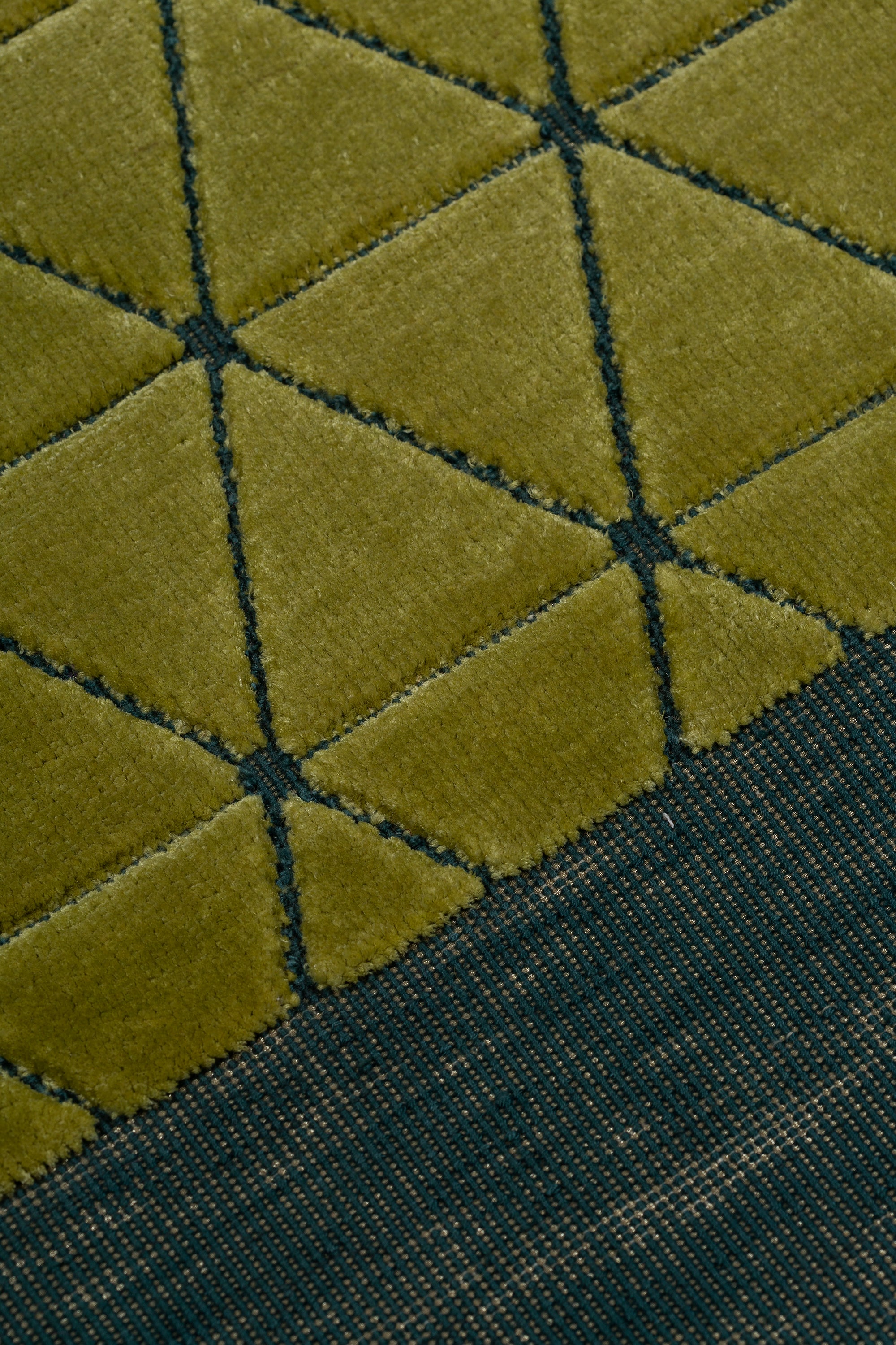 Detail of the Bucky Rug in citrine-jade, features a wide dark sage green border with a chartreuse colored lattice field with a metallic sheen. 