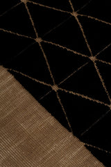 Detail of the Bucky Rug in jet-tan, features a wide taupe border with a black lattice field with a metallic sheen. 