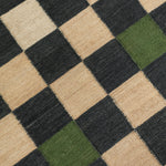 Detail of the Checkerboard Rug in King, a black and tan checkered pattern with random accents of green and white. 