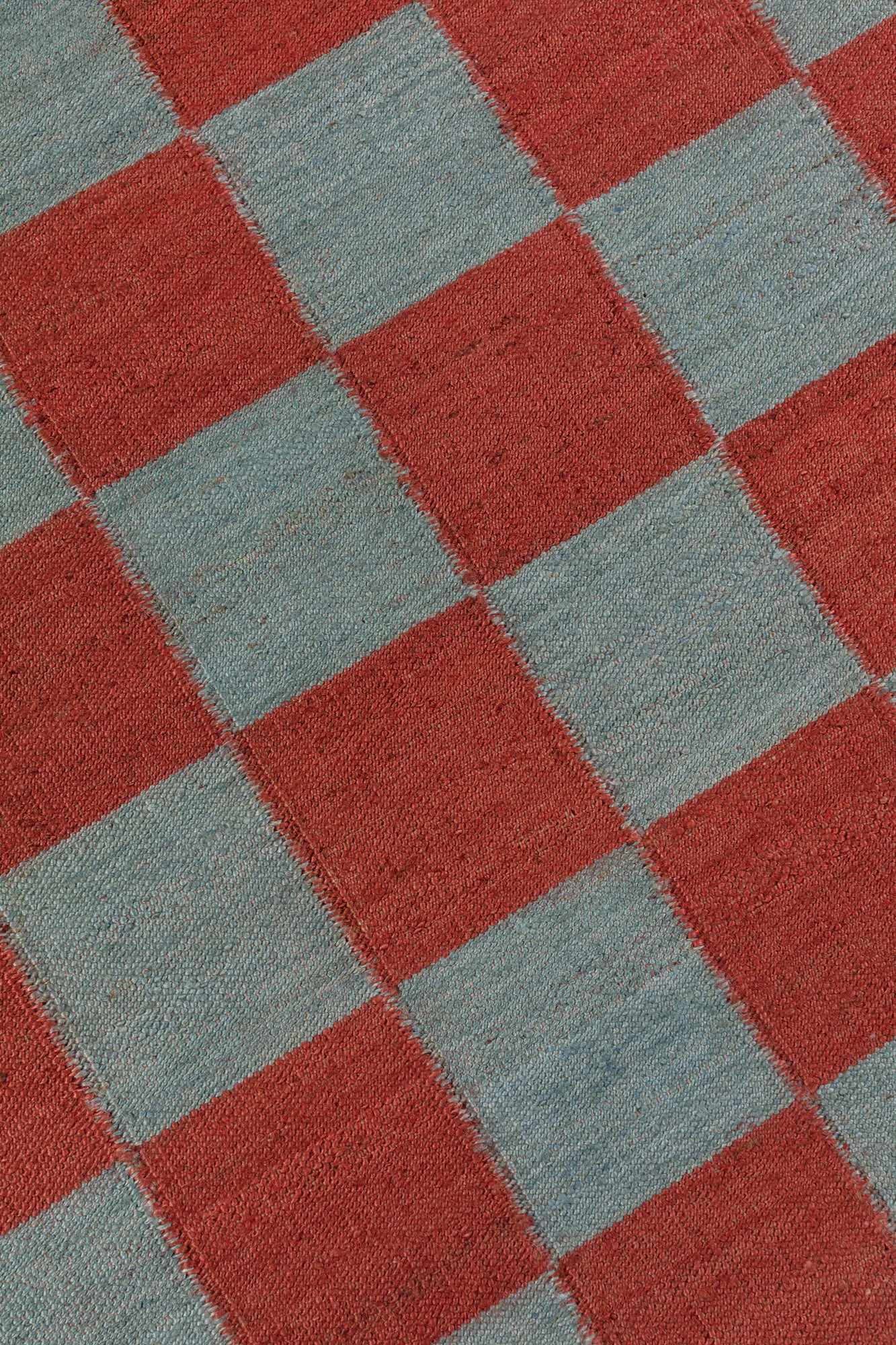 Detail of the Checkerboard Rug in Pawn, a red and sky blue checkered pattern. 