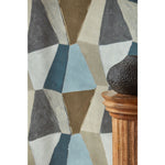 detail image of a black vase and wood column in front Detail swatch of a wallpaper pattern with mixed three dimensional diamond forms with black, white, beige, chocolate brown, sky blue and petrol blue on a textured paper, hover