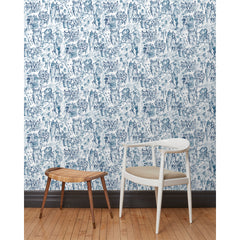 A chair and stool stand in front of a wall papered in repeating watercolor illustrations of horses, farmers and country houses in navy on a white background.