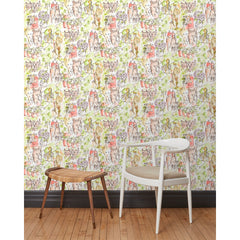 A chair and stool stand in front of a wall papered in repeating watercolor illustrations of horses, farmers and country houses in green and pink on a white background.