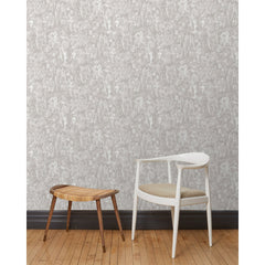 A chair and stool stand in front of a wall papered in repeating watercolor illustrations of horses, farmers and country houses in white on a tan background.