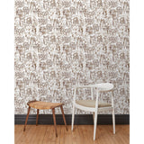 A chair and stool stand in front of a wall papered in repeating watercolor illustrations of horses, farmers and country houses in sepia on a white background.