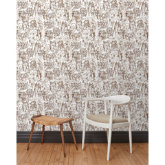 A chair and stool stand in front of a wall papered in repeating watercolor illustrations of horses, farmers and country houses in sepia on a white background.