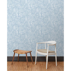 A chair and stool stand in front of a wall papered in repeating watercolor illustrations of horses, farmers and country houses in white on a blue background.