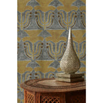 An ornate silver tear drop filigree lamp on a ornate carved wooden table in front of a wallpaper with stamped painted floral motif in yellow and brown on a grey background, hover