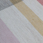 Detail of the Jasper Waffle Rug in Red Fossile, widely spaced stripes of yellow, pink, red, white and black on a split light grey fand ivory field. 