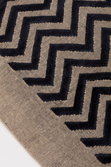 Detail of the Penta Chevron Rug in Jet, a black chevron pattern on a taupe field with a wide solid border. 
