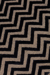 Detail of the Penta Chevron Rug in Jet, a black chevron pattern on a taupe field with a wide solid border. 