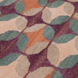 Detail of the Petite Alhambra Rug featuring a pattern of linked circles that create a star like lattice in coral, taupe, turquoise and royal purple. 