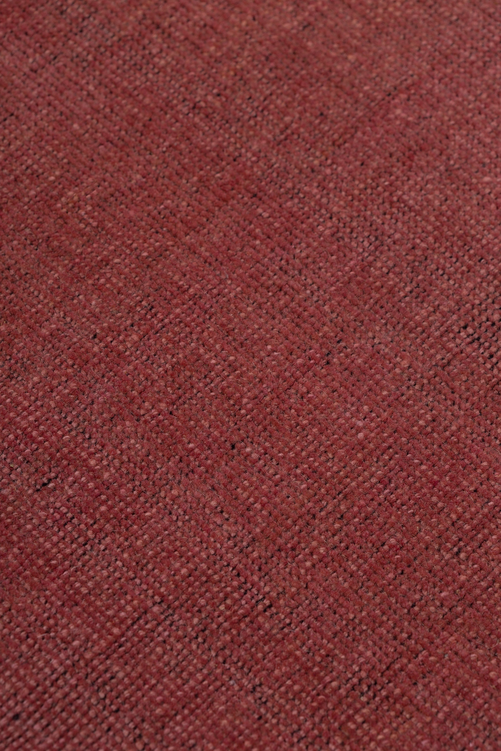 Detail of the Plain Stitched Border Rug in Carmine, a solid red rug with a black border with black border with pink and taupe dashes. 
