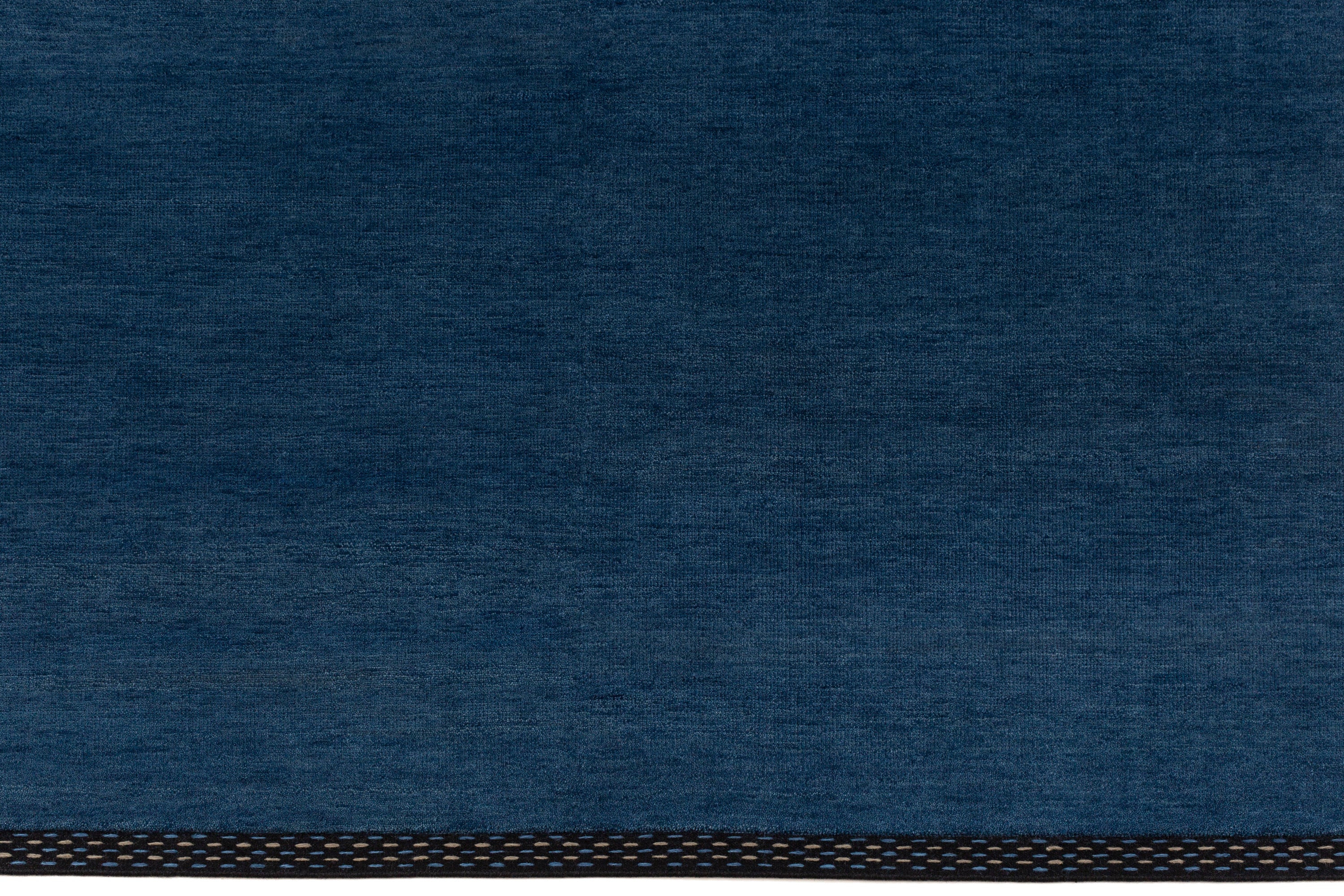 Detail of the Plain Stitched Border Rug in Prussian Blue, a solid indigo rug with a black border with black border with blue and taupe dashes. 