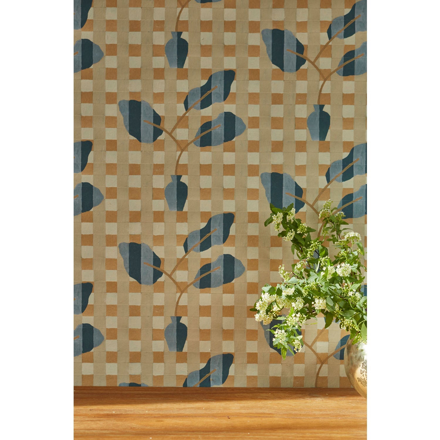 A small white and green floral arrangement at the left edge of the frame against a wallpaper with a complex cornflower and dark blue striped floral motif overlayed a white and tan plaid pattern, hover