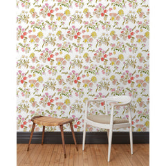 A chair and stool stand in front of a wall papered in large-scale line-drawn flowers in gray ink with red, pink and yellow watercolors, on a beige background.