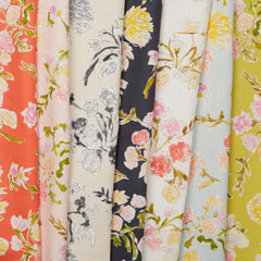 A row of folded linen fabrics, all in the same large-scale line-drawn floral print in various shades of red, pink, blue and green.