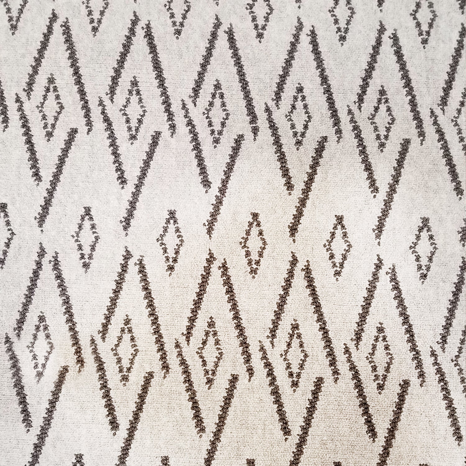Woven broadloom carpet swatch in a repeating irregular diamond pattern in charcoal on a tan field.