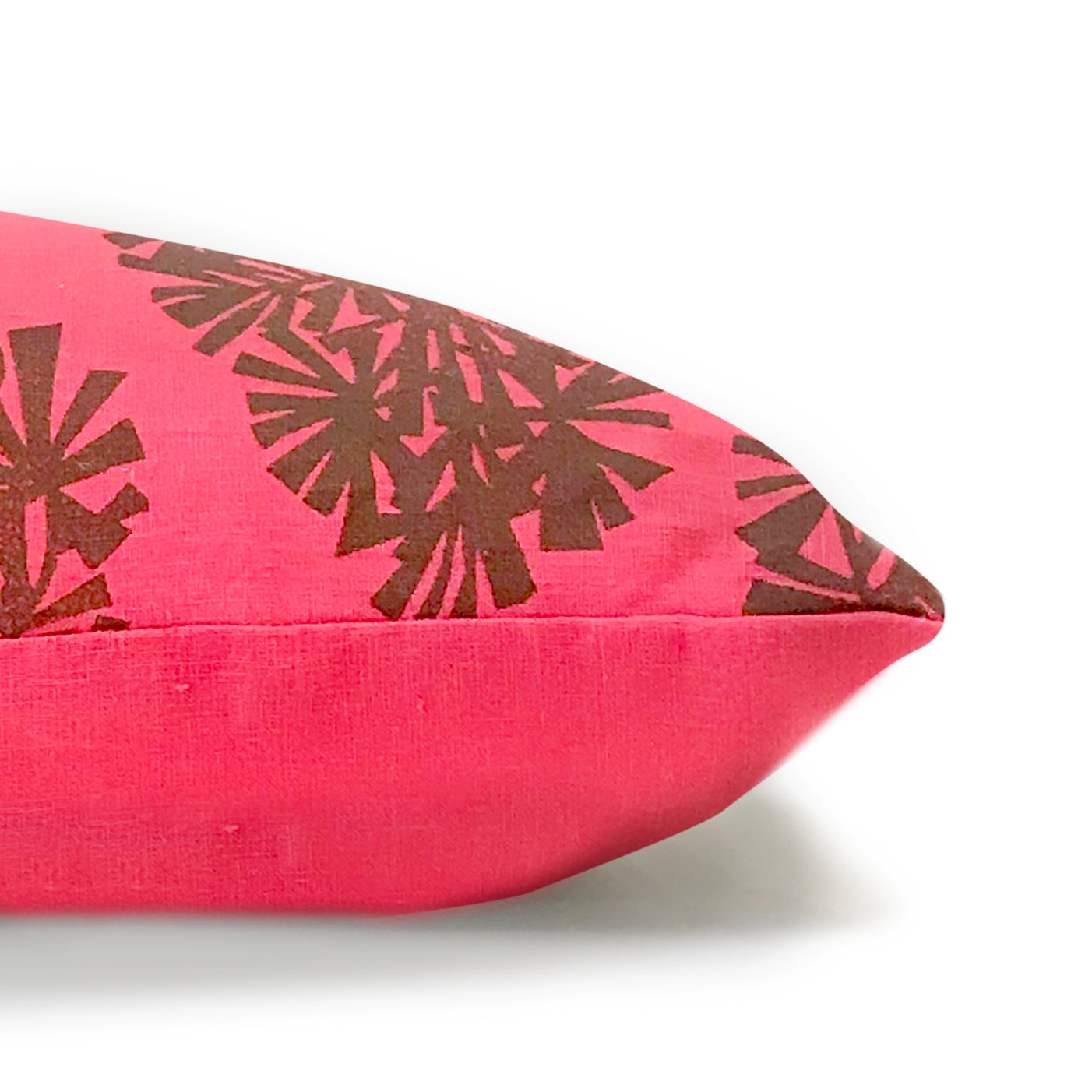 Side view of a throw pillow in pink. One side is printed in a repeating brown geometric pattern.