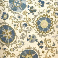 Woven rug swatch in a floral pattern in shades of blue, green and gray on a cream field.