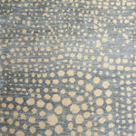 Woven rug swatch in a pattern of many repeating different-sized circles in tan on a blue-gray field.