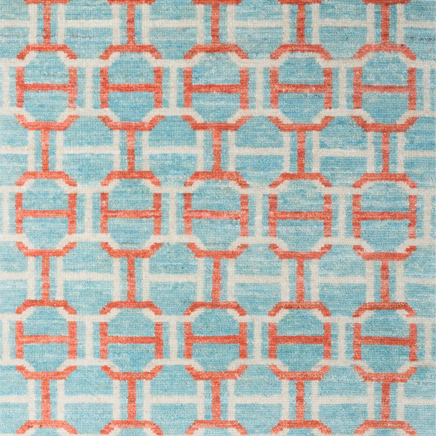 Woven rug swatch in an interlocking geometric buckle pattern in coral and white on a light blue field.