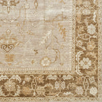 Woven rug swatch with a repeating abstract foral pattern and a dense floral border in shades of white, tan and brown.