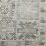 Woven rug swatch in a repeating abstract geometric pattern with a border of jagged geometric shapes, all in shades of gray.