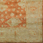 Woven rug swatch with a minimalist floral pattern in tan on a red field, with a tan border of linear florals in red.