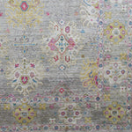 Detail of a woven rug in an abstract floral pattern with a repeating floral border print in shades of pink, yellow and red on a mottled gray field.