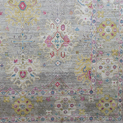 Detail of a woven rug in an abstract floral pattern with a repeating floral border print in shades of pink, yellow and red on a mottled gray field.