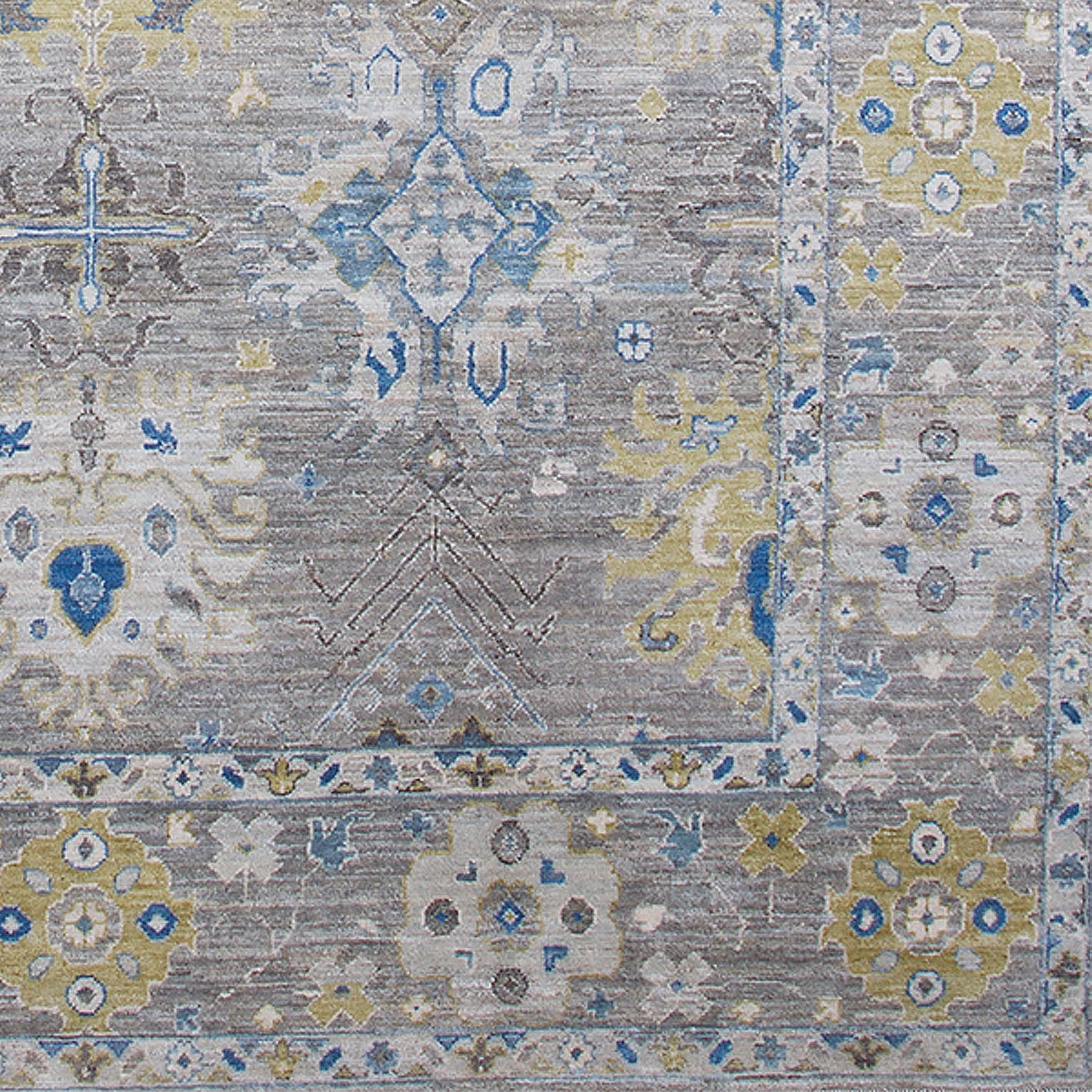 Detail of a woven rug in an abstract floral pattern with a repeating floral border print in shades of yellow, blue and gray on a mottled gray field.