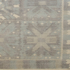 Woven rug swatch in a repeating abstract geometric pattern with a border of jagged geometric shapes, all in shades of gray.