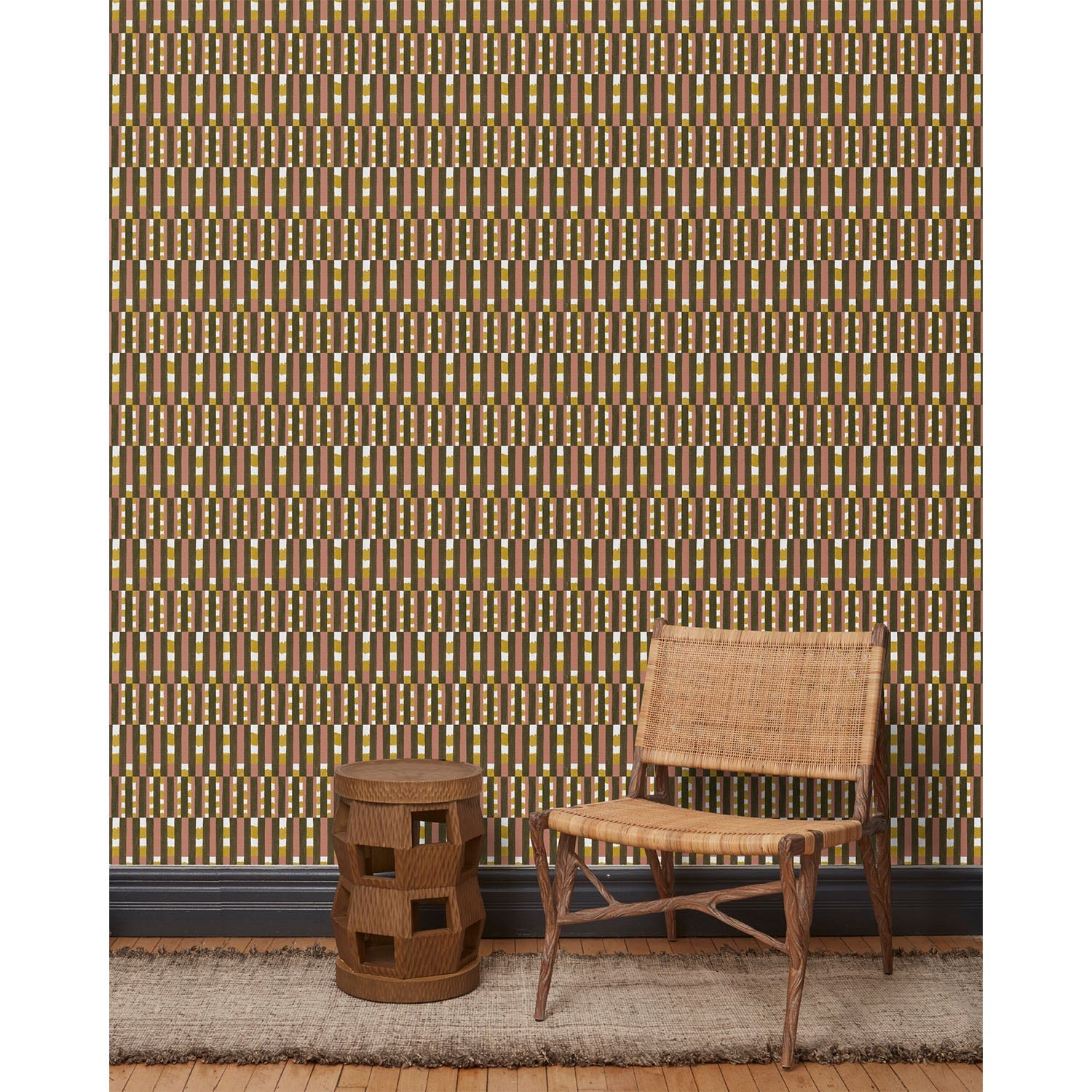 Wood and woven chair, brown stool and rug in front of wallpaper with a pattern of vertical stripes of pink, warm olive green and dashes of yellow and white, hover