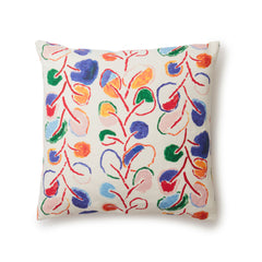 A square throw pillow with repeating rows of colorful leaf prints in shades of red, purple and blue on a cream background.