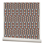 Wallpaper roll with a pattern of vertical stripes of light brown, navy blue and dashes of rust red and white.