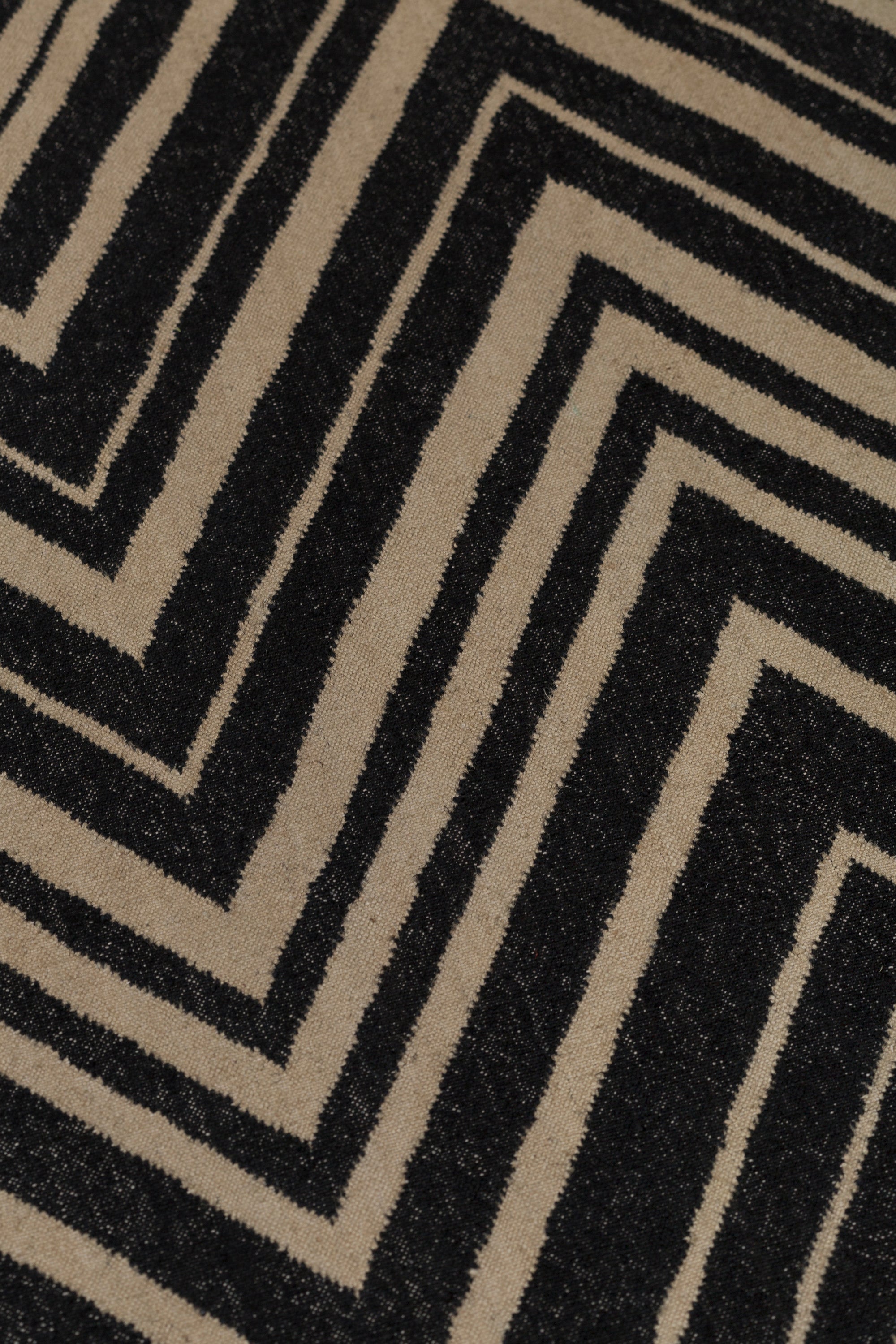 Detail of the Vertical Zig-Zag Rug in Onyx-Sandstone, a zig zag pattern in mixed widths in black and taupe.