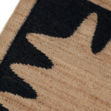 Detail of the Waver Rug in Jet Black, a strated ecru field with a black flame stitch border. 
