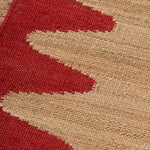 Detail of the Waver Rug in Safflower Red, a strated ecru field with a red flame stitch border. 