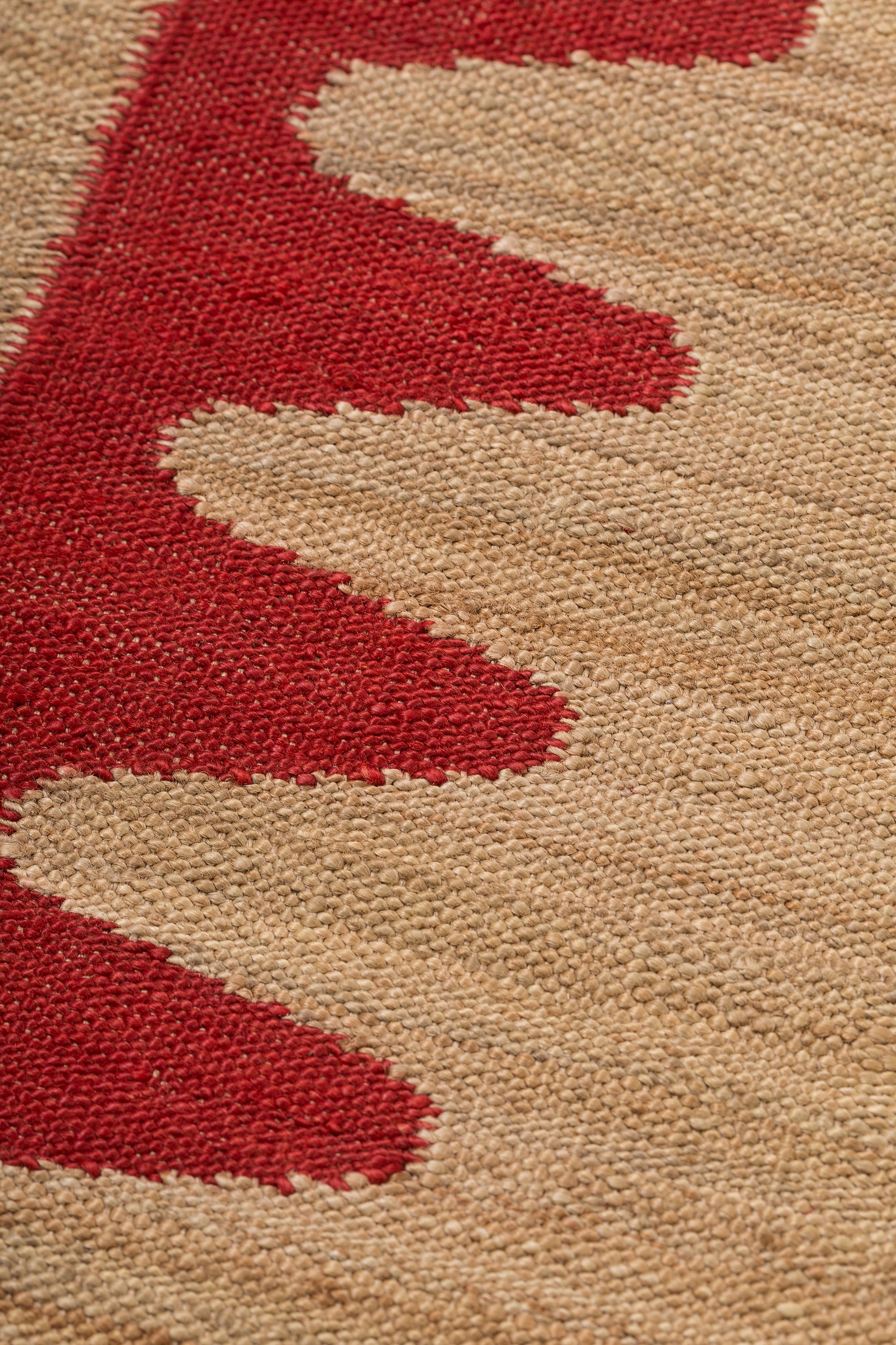 Detail of the Waver Rug in Safflower Red, a strated ecru field with a red flame stitch border. 