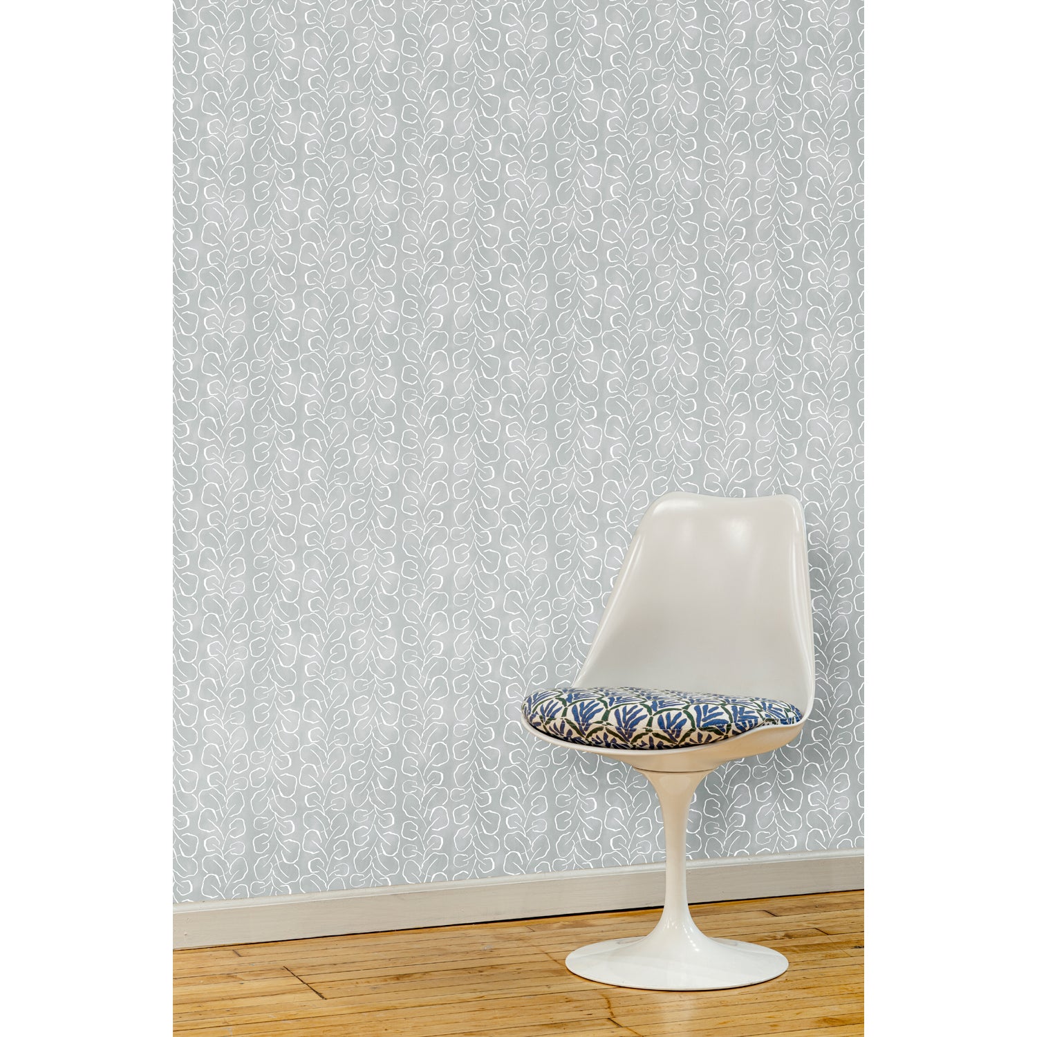 A white swivel chair in front of a wall papered in a large-scale repeating leaf print in white on a blue-gray watercolor background.