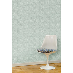 A white swivel chair in front of a wall papered in a large-scale repeating leaf print in white on a sage green watercolor background.